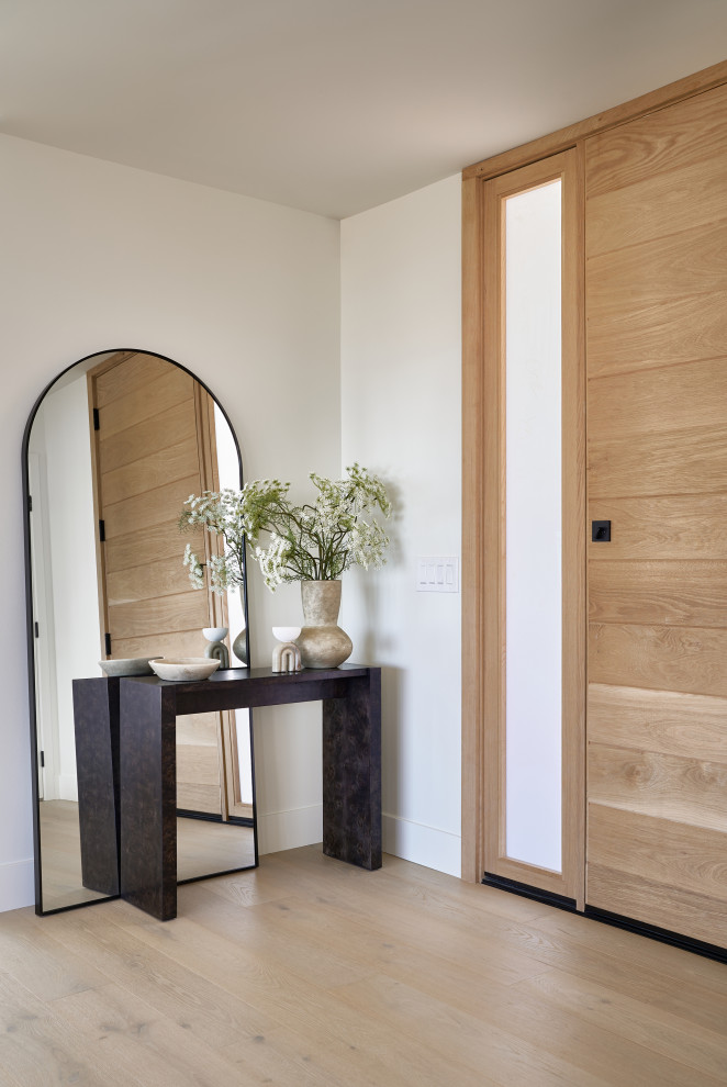 Ispirazione per un piccolo ingresso design con pareti bianche, una porta a pivot, una porta in legno chiaro e pavimento beige
