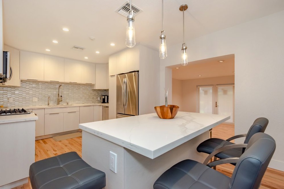 Photo of a small modern u-shaped eat-in kitchen in Other with an undermount sink, flat-panel cabinets, white cabinets, quartz benchtops, white splashback, glass tile splashback, stainless steel appliances, light hardwood floors, with island, orange floor and white benchtop.