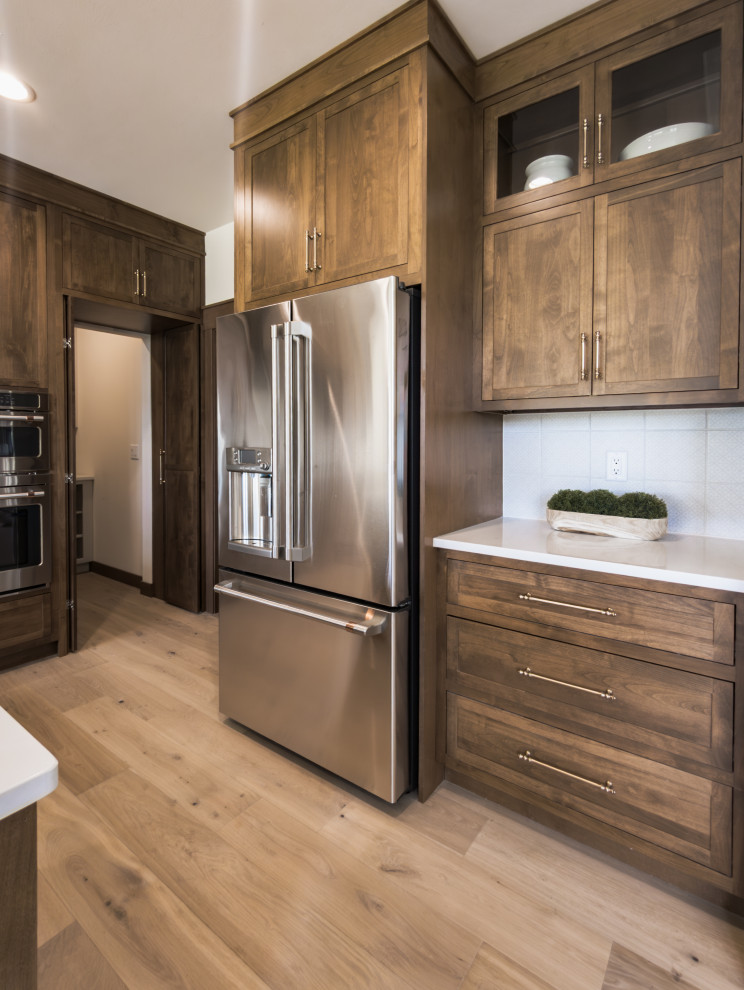 Open concept kitchen - transitional galley light wood floor and beige floor open concept kitchen idea with shaker cabinets, medium tone wood cabinets, quartz countertops, white backsplash, porcelain backsplash, stainless steel appliances, an island and white countertops