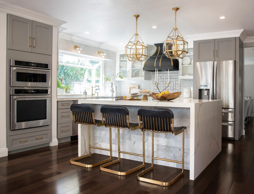 Transitional l-shaped dark wood floor and brown floor kitchen photo in Orange County with a farmhouse sink, shaker cabinets, gray cabinets, gray backsplash, stainless steel appliances and an island