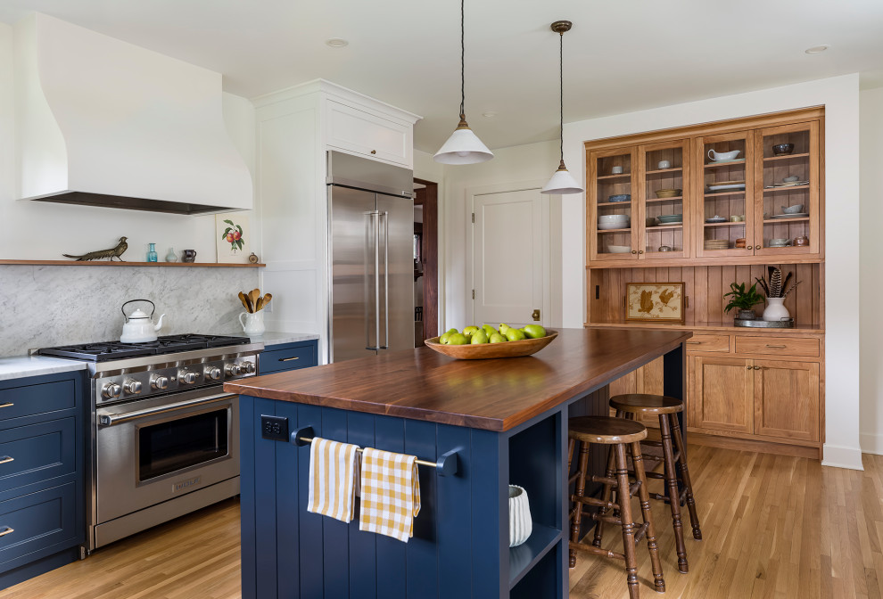 Inspiration for a mid-sized country l-shaped separate kitchen in Minneapolis with an undermount sink, recessed-panel cabinets, blue cabinets, wood benchtops, white splashback, marble splashback, stainless steel appliances, medium hardwood floors, with island, white floor and brown benchtop.