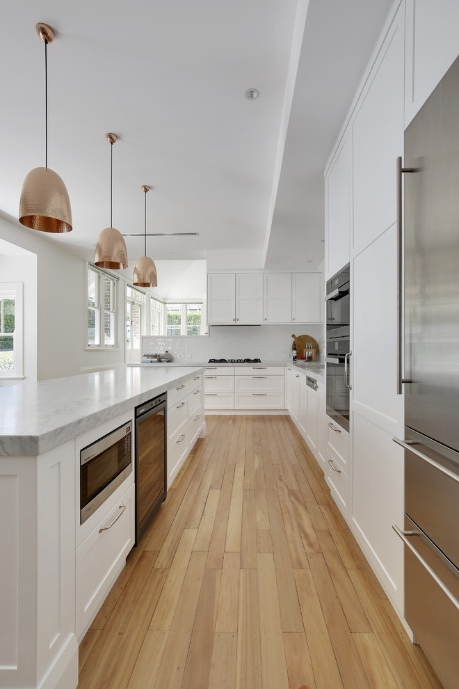 Photo of a large traditional l-shaped eat-in kitchen in Sydney with a double-bowl sink, shaker cabinets, white cabinets, marble benchtops, white splashback, ceramic splashback, stainless steel appliances, light hardwood floors, with island and yellow floor.