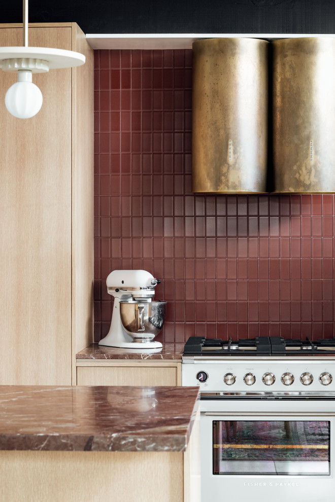 Bild på ett mellanstort 50 tals röd rött kök, med en integrerad diskho, släta luckor, skåp i ljust trä, marmorbänkskiva, rött stänkskydd, stänkskydd i glaskakel, vita vitvaror, terrazzogolv, en halv köksö och grått golv