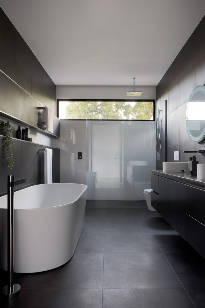 Design ideas for a mid-sized contemporary master bathroom in Melbourne with flat-panel cabinets, black cabinets, a freestanding tub, gray tile, a vessel sink, grey benchtops, a double vanity, a floating vanity, a niche, an alcove shower, a wall-mount toilet, porcelain tile, black walls, porcelain floors, engineered quartz benchtops, black floor and an open shower.