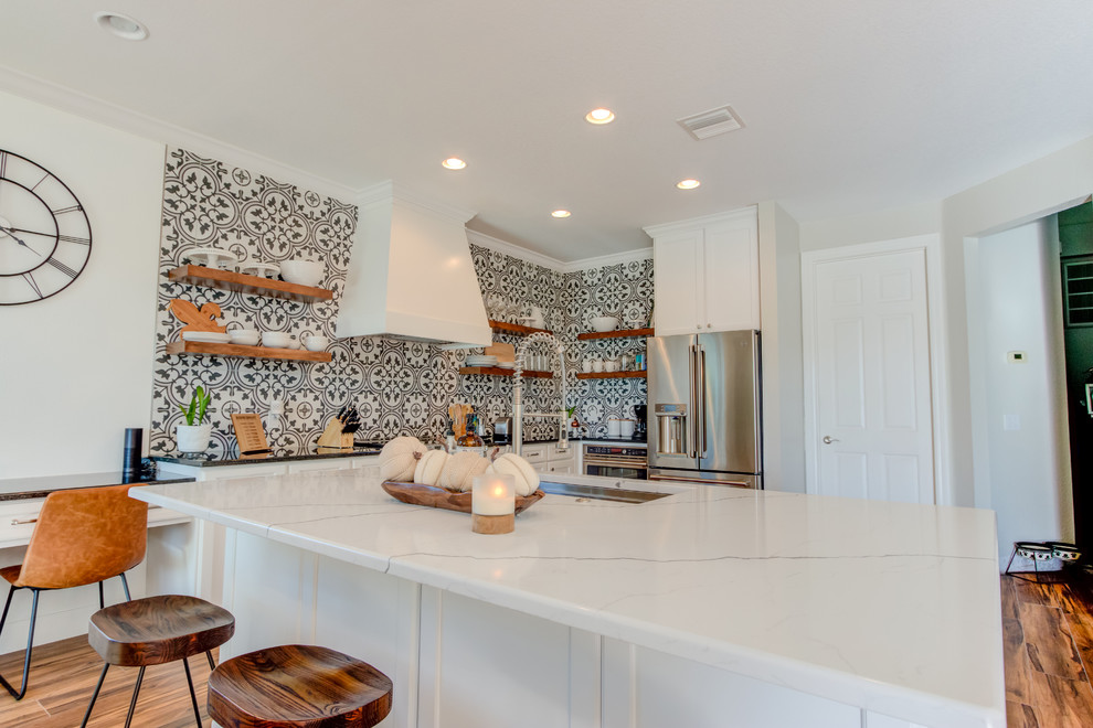 Large transitional l-shaped ceramic tile and brown floor eat-in kitchen photo with an undermount sink, shaker cabinets, white cabinets, quartz countertops, multicolored backsplash, ceramic backsplash, stainless steel appliances, an island and white countertops