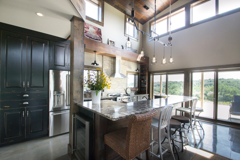 Example of a mountain style galley concrete floor eat-in kitchen design in Cedar Rapids with an island, raised-panel cabinets, black cabinets, granite countertops, beige backsplash, stone tile backsplash and stainless steel appliances