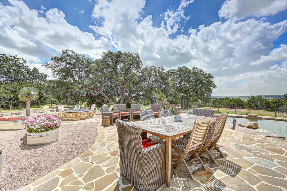 This is an example of a large country backyard kidney-shaped natural pool in Austin with a hot tub and natural stone pavers.