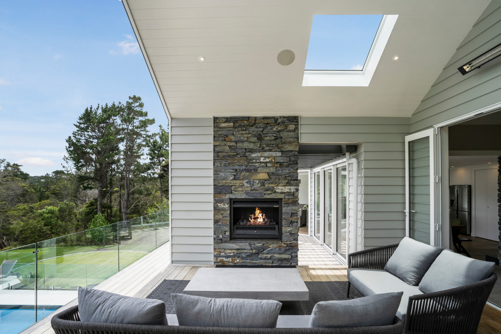 This is an example of a mid-sized contemporary balcony in Auckland with with fireplace, a roof extension and glass railing.