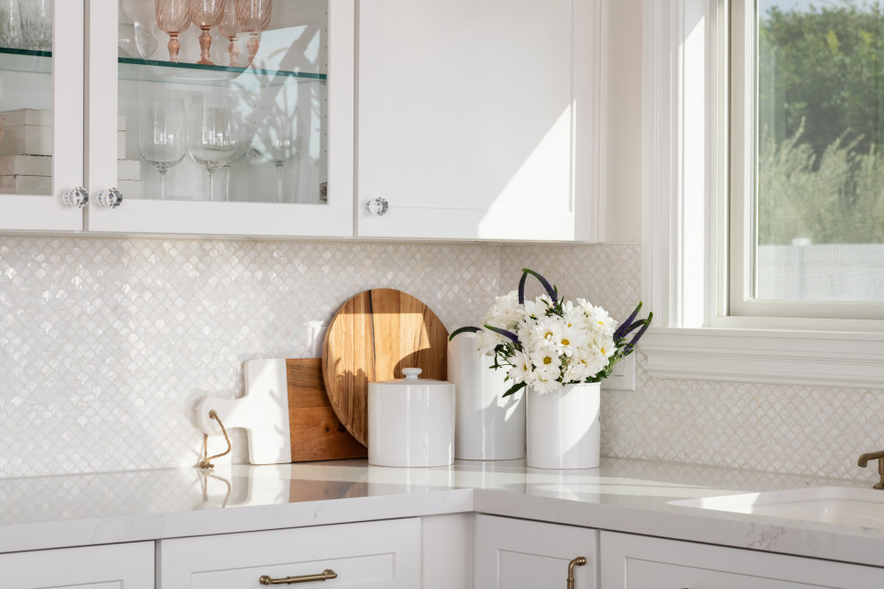 Maritim inredning av ett litet vit vitt kök, med en integrerad diskho, skåp i shakerstil, vita skåp, bänkskiva i kvarts, vitt stänkskydd, stänkskydd i mosaik, rostfria vitvaror och en halv köksö