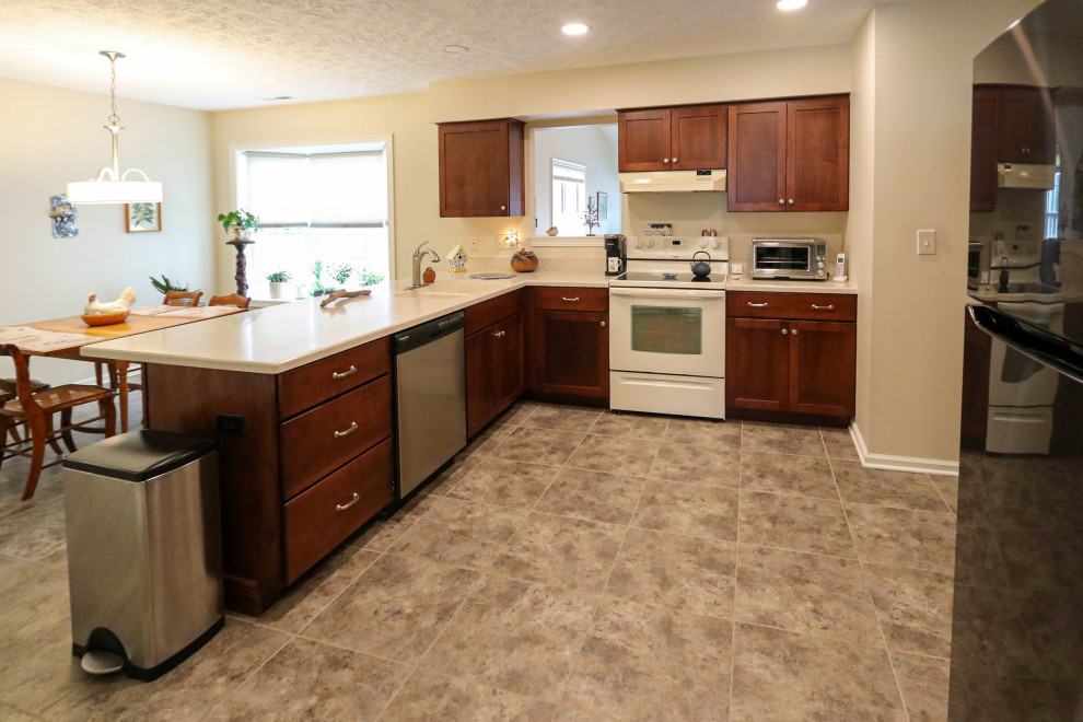 This is an example of a mid-sized transitional l-shaped eat-in kitchen in Cleveland with an undermount sink, raised-panel cabinets, brown cabinets, solid surface benchtops, white appliances, porcelain floors, a peninsula, beige floor and beige benchtop.