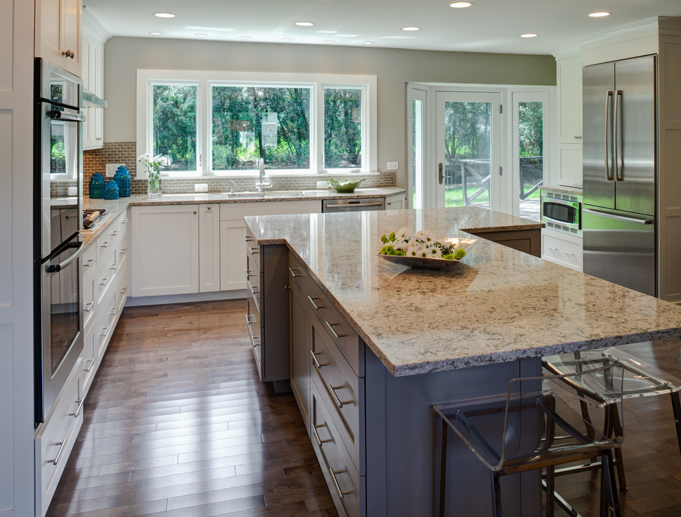 This is an example of a transitional l-shaped eat-in kitchen in Chicago with shaker cabinets, quartz benchtops, glass tile splashback, stainless steel appliances, a double-bowl sink and grey cabinets.