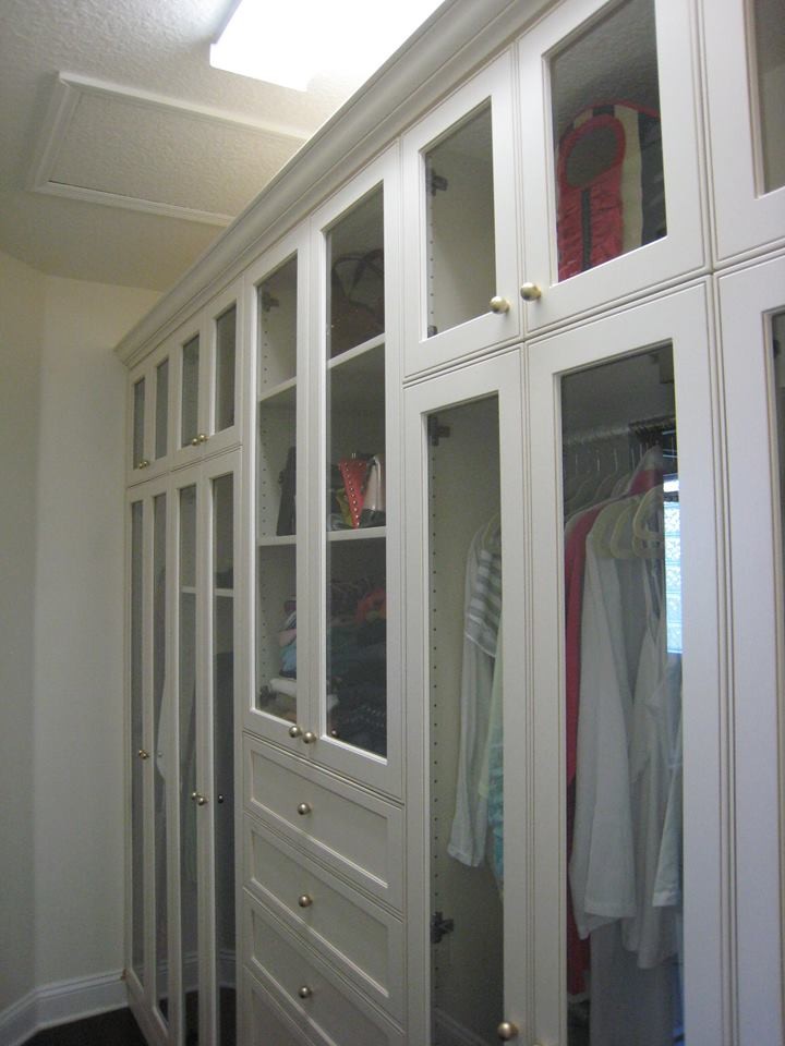 Photo of a mid-sized transitional walk-in wardrobe in Jacksonville with glass-front cabinets, white cabinets, dark hardwood floors and brown floor.
