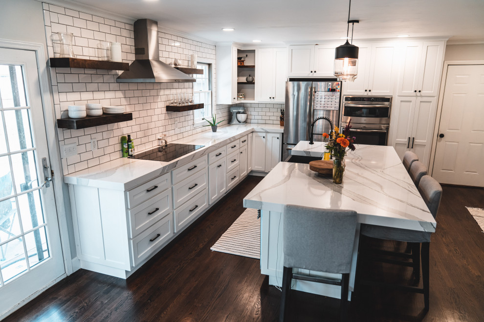 Photo of a large country l-shaped eat-in kitchen in Other with a farmhouse sink, shaker cabinets, white cabinets, quartz benchtops, white splashback, subway tile splashback, stainless steel appliances, dark hardwood floors, with island, brown floor and white benchtop.