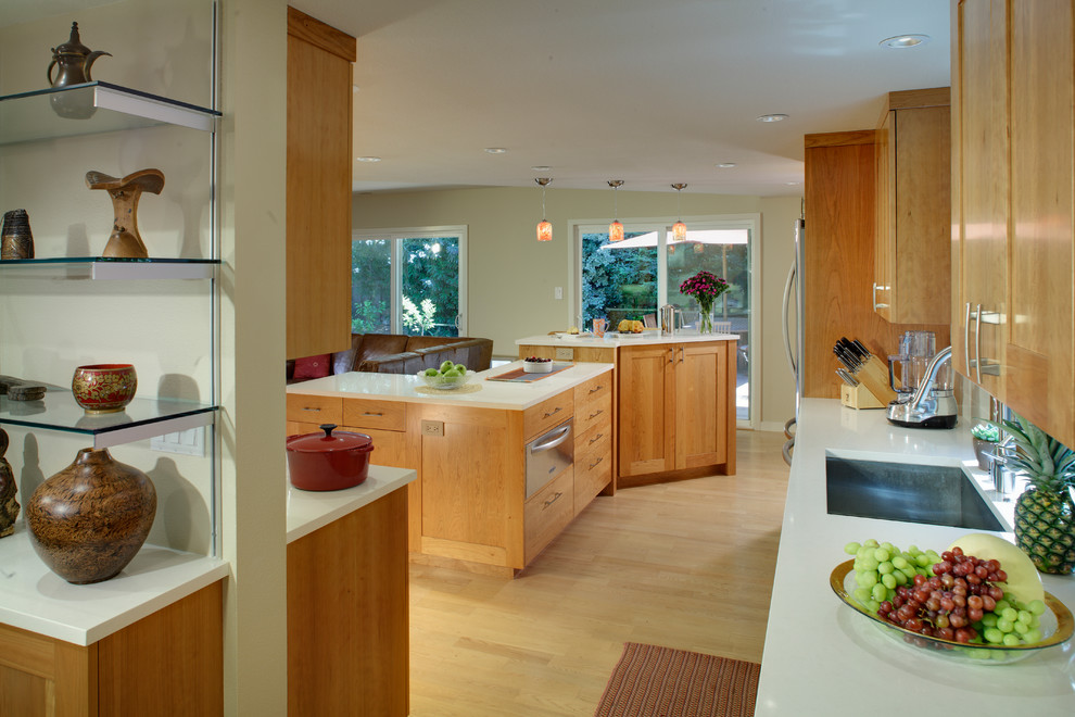 Mid-sized contemporary l-shaped open plan kitchen in Sacramento with an undermount sink, shaker cabinets, medium wood cabinets, solid surface benchtops, white splashback, matchstick tile splashback, stainless steel appliances, medium hardwood floors, with island and beige floor.