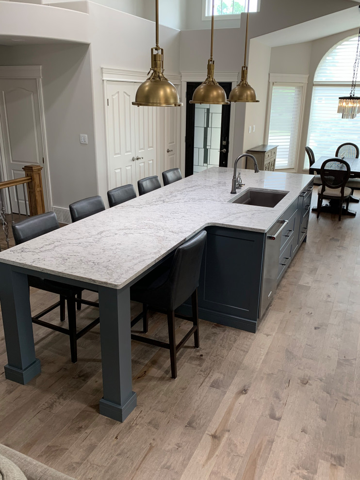 Example of a large transitional galley light wood floor, brown floor and vaulted ceiling eat-in kitchen design with an undermount sink, shaker cabinets, white cabinets, quartzite countertops, white backsplash, ceramic backsplash, stainless steel appliances, an island and white countertops
