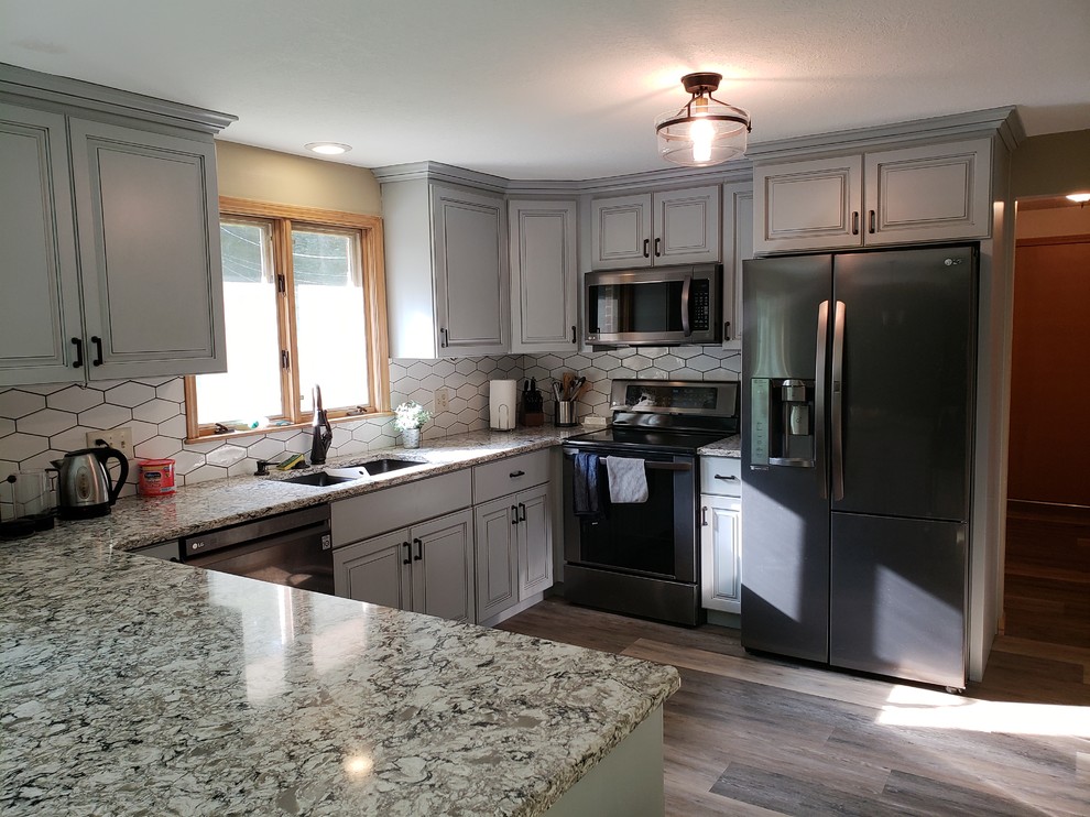 Eat-in kitchen - mid-sized transitional u-shaped medium tone wood floor and brown floor eat-in kitchen idea with an undermount sink, raised-panel cabinets, gray cabinets, granite countertops, white backsplash, ceramic backsplash, stainless steel appliances, a peninsula and multicolored countertops