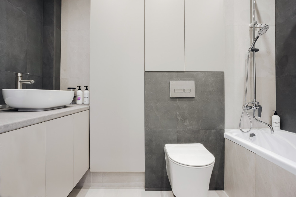 Foto på ett mellanstort funkis grå en-suite badrum, med släta luckor, grå skåp, ett platsbyggt badkar, en dusch/badkar-kombination, en vägghängd toalettstol, grå kakel, klinkergolv i keramik, ett fristående handfat, grått golv och med dusch som är öppen