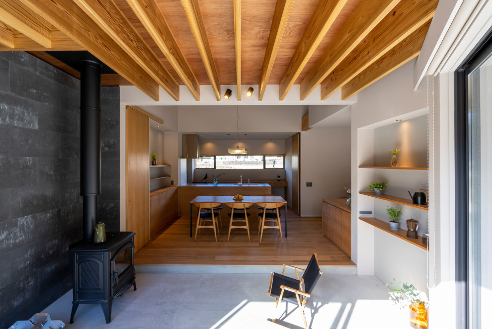 Aménagement d'une salle à manger ouverte sur le salon moderne avec un mur blanc, sol en béton ciré, un poêle à bois, un manteau de cheminée en béton, un sol gris, poutres apparentes et du papier peint.