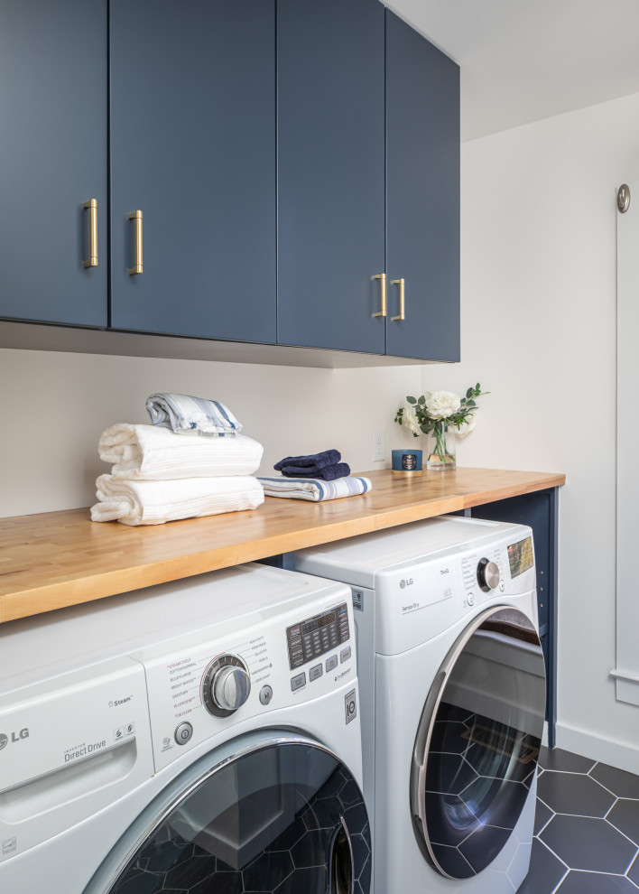 This is an example of a small contemporary single-wall dedicated laundry room in Raleigh with flat-panel cabinets, blue cabinets, wood benchtops, white walls, ceramic floors, a side-by-side washer and dryer, black floor and brown benchtop.