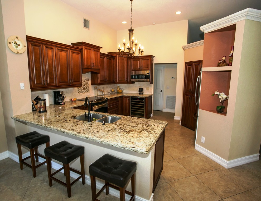 Mid-sized transitional u-shaped porcelain tile eat-in kitchen photo in Miami with an undermount sink, raised-panel cabinets, brown cabinets, granite countertops, beige backsplash, stone tile backsplash, stainless steel appliances, beige walls and a peninsula