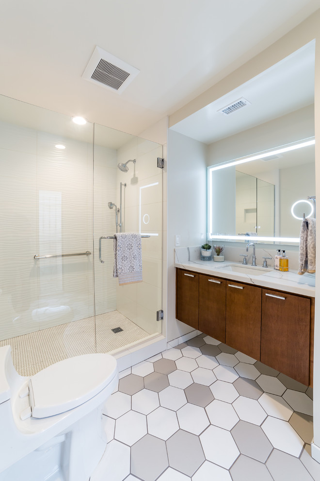 This is an example of a large midcentury master bathroom in San Diego with shaker cabinets, brown cabinets, an alcove shower, a two-piece toilet, white tile, glass sheet wall, beige walls, ceramic floors, an undermount sink, granite benchtops, multi-coloured floor, a hinged shower door and white benchtops.