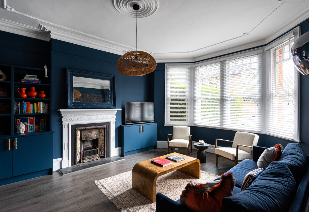 This is an example of a contemporary enclosed living room in London with blue walls, dark hardwood flooring, a standard fireplace, a freestanding tv and brown floors.