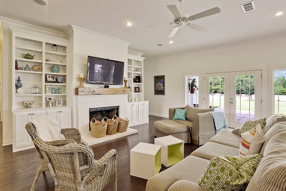 Photo of a large beach style open concept living room in New Orleans with white walls, dark hardwood floors, a standard fireplace, a brick fireplace surround and a wall-mounted tv.