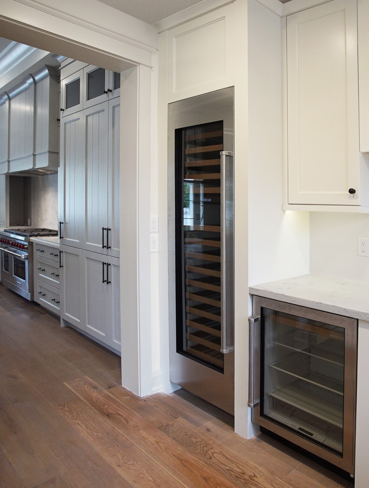 Large traditional l-shaped eat-in kitchen in Phoenix with a farmhouse sink, louvered cabinets, grey cabinets, quartzite benchtops, white splashback, stone slab splashback, white appliances, dark hardwood floors, with island and brown floor.