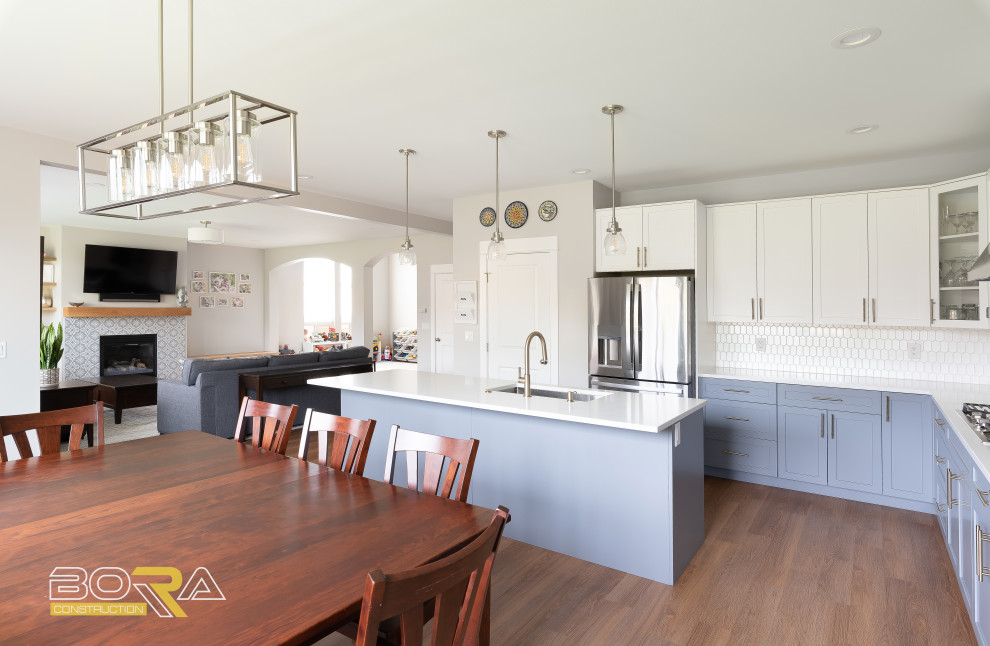 Eat-in kitchen - large transitional l-shaped medium tone wood floor and brown floor eat-in kitchen idea in Seattle with an undermount sink, shaker cabinets, blue cabinets, quartz countertops, white backsplash, ceramic backsplash, stainless steel appliances, an island and white countertops