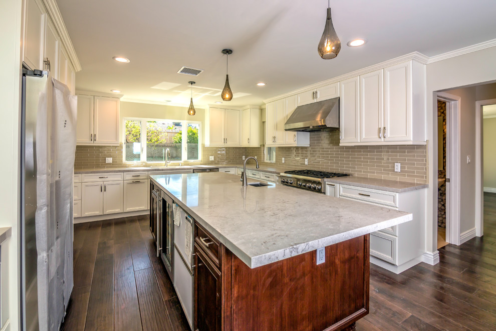 Large transitional u-shaped eat-in kitchen in San Francisco with an undermount sink, recessed-panel cabinets, white cabinets, beige splashback, glass tile splashback, stainless steel appliances, dark hardwood floors and with island.