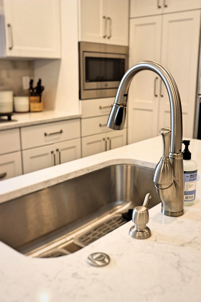 Transitional l-shaped medium tone wood floor and brown floor kitchen pantry photo in Cedar Rapids with an undermount sink, recessed-panel cabinets, white cabinets, quartzite countertops, gray backsplash, porcelain backsplash, stainless steel appliances, an island and white countertops