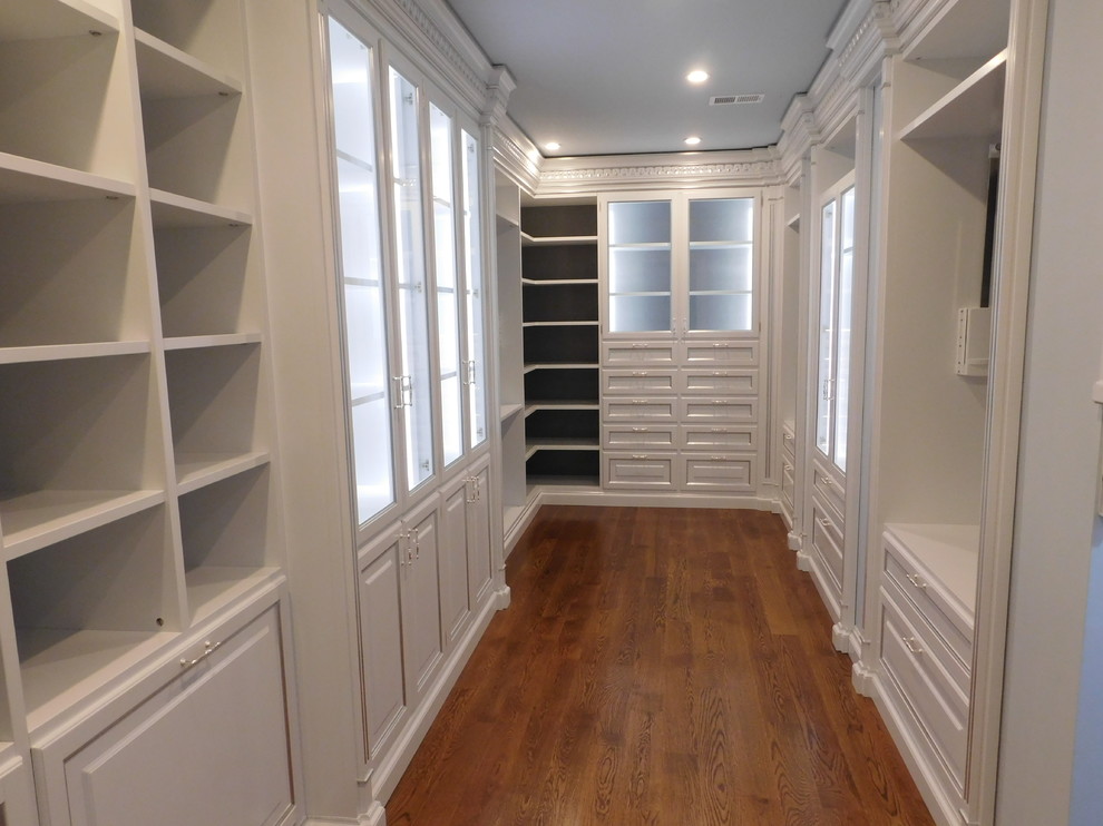 Photo of a large mediterranean women's walk-in wardrobe in DC Metro with glass-front cabinets, white cabinets and medium hardwood floors.