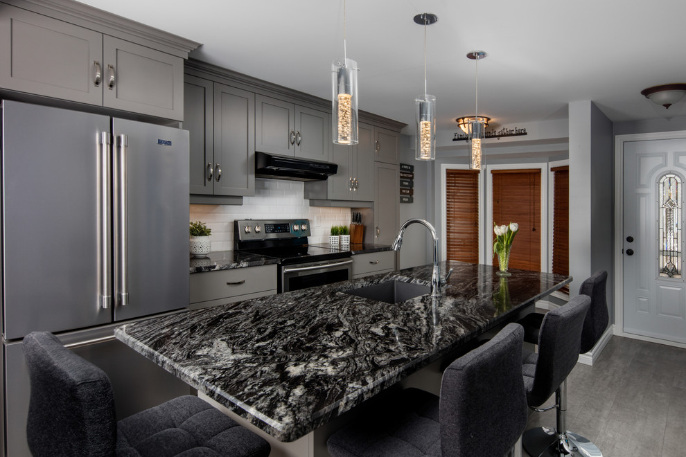 Kitchen - gray floor kitchen idea in Toronto with shaker cabinets, gray cabinets, white backsplash, subway tile backsplash, stainless steel appliances, an island and black countertops