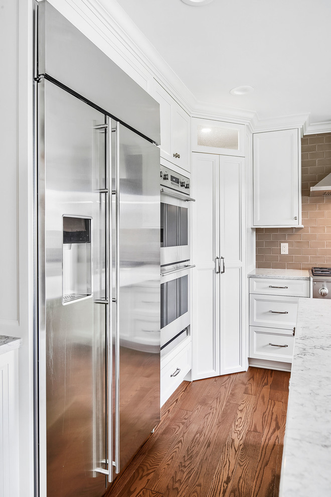 Kitchen pantry - mid-sized transitional u-shaped medium tone wood floor and brown floor kitchen pantry idea in Detroit with an undermount sink, shaker cabinets, white cabinets, quartz countertops, beige backsplash, porcelain backsplash, stainless steel appliances, an island and beige countertops
