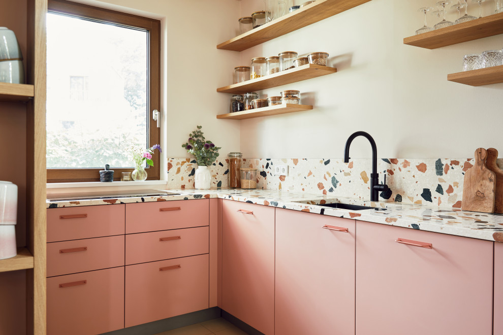 На фото: узкая отдельная, угловая кухня в современном стиле с плоскими фасадами, розовыми фасадами, столешницей терраццо, бежевым фартуком и разноцветной столешницей без острова