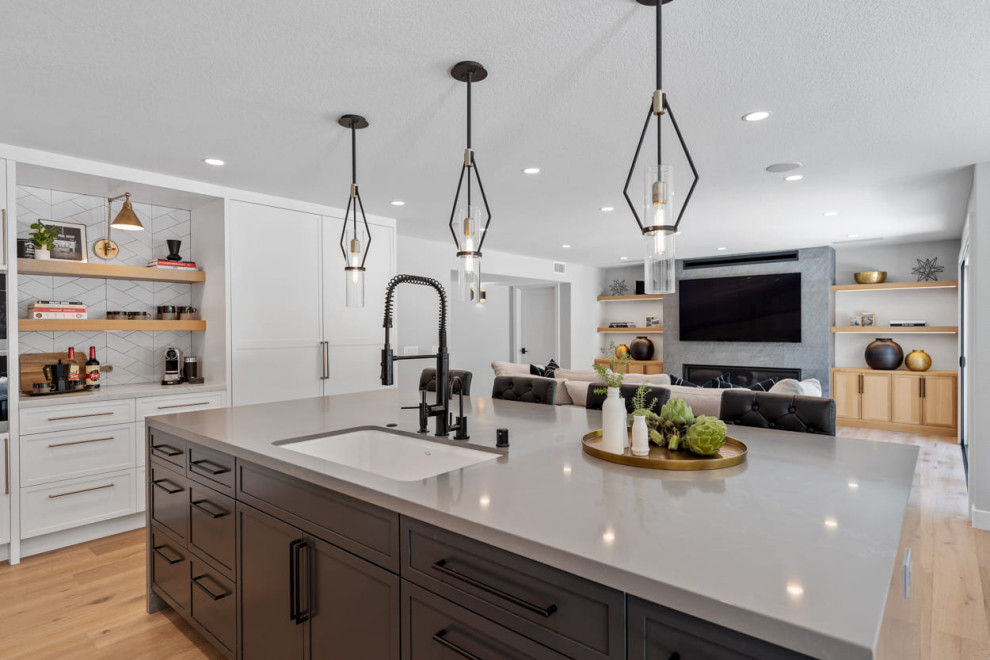 Design ideas for an expansive modern open plan kitchen in Los Angeles with a single-bowl sink, shaker cabinets, white cabinets, quartzite benchtops, white splashback, porcelain splashback, stainless steel appliances, light hardwood floors, with island and grey benchtop.