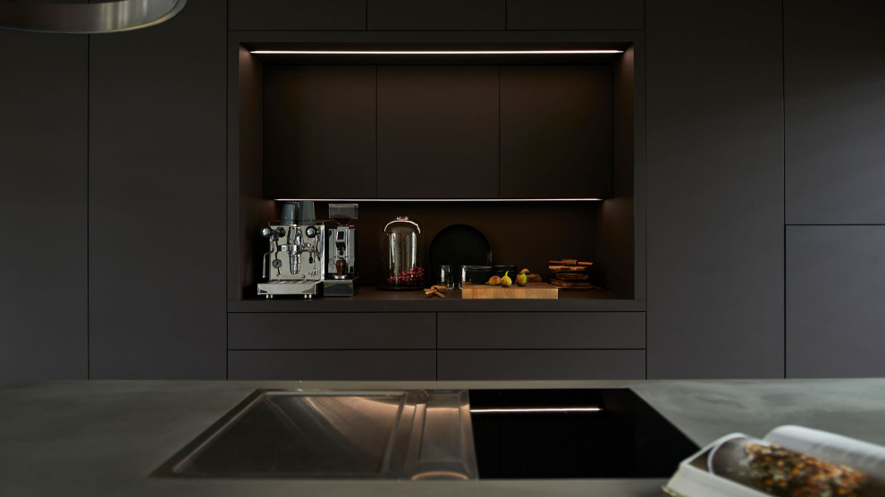 Cette photo montre une cuisine ouverte tendance avec des portes de placard noires, une crédence noire, sol en béton ciré et îlot.