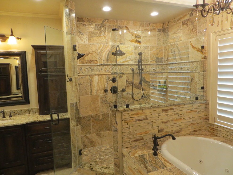 Large mountain style master brown tile and stone tile ceramic tile drop-in bathtub photo in Dallas with an undermount sink, raised-panel cabinets, dark wood cabinets, granite countertops, a two-piece toilet and beige walls