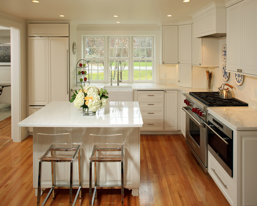 Example of a mid-sized transitional l-shaped medium tone wood floor eat-in kitchen design in Boston with white cabinets, an island, a farmhouse sink, raised-panel cabinets, marble countertops, white backsplash, glass sheet backsplash and stainless steel appliances