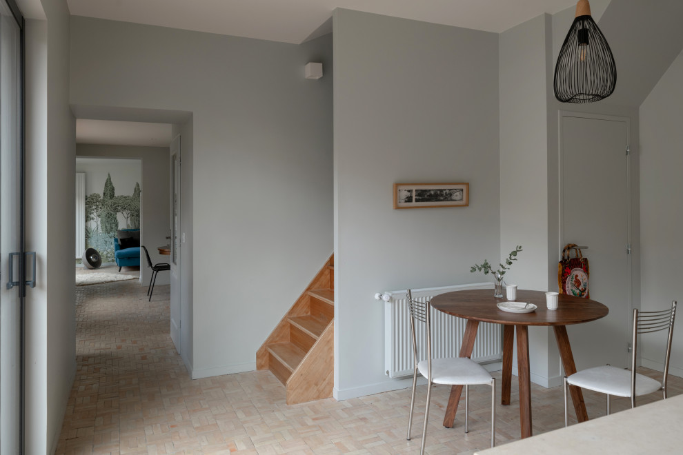 Immagine di una grande sala da pranzo aperta verso il soggiorno con pareti grigie, pavimento in terracotta, pavimento beige e carta da parati