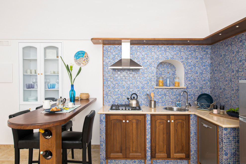Photo of a mid-sized mediterranean l-shaped eat-in kitchen in Other with a single-bowl sink, raised-panel cabinets, medium wood cabinets, multi-coloured splashback, stainless steel appliances, a peninsula, beige benchtop, marble benchtops, mosaic tile splashback, ceramic floors, beige floor and vaulted.
