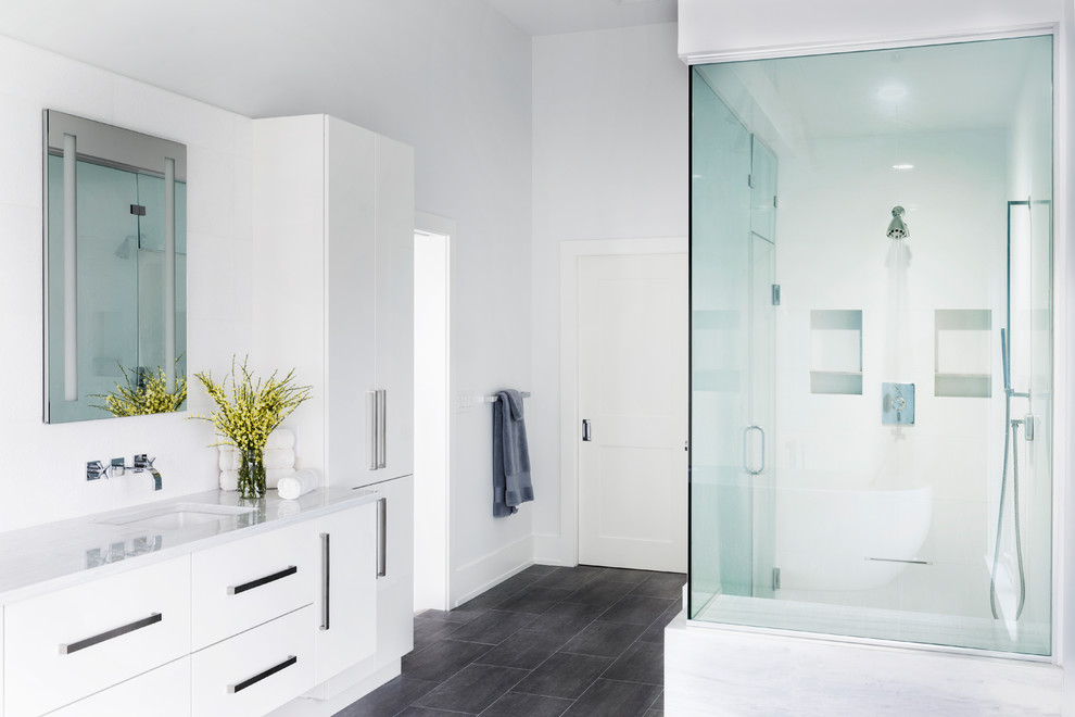 Mid-sized beach style master bathroom in New York with flat-panel cabinets, white cabinets, a freestanding tub, an alcove shower, white tile, white walls, porcelain floors, an undermount sink, grey floor and a hinged shower door.