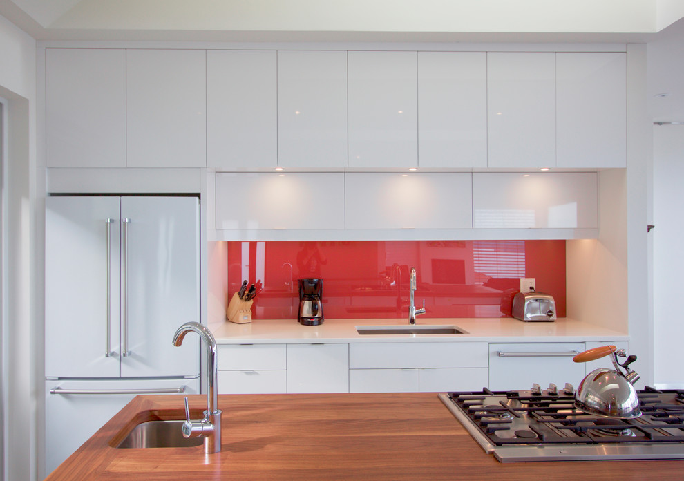 Design ideas for a mid-sized modern single-wall eat-in kitchen in Other with an undermount sink, flat-panel cabinets, white cabinets, wood benchtops, red splashback, glass sheet splashback, white appliances, concrete floors, with island, grey floor and brown benchtop.