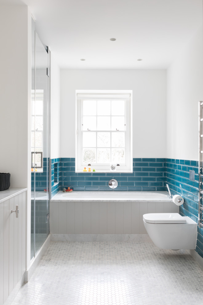 Design ideas for a mid-sized transitional bathroom in London with grey cabinets, a wall-mount toilet, white walls, white floor, a hinged shower door, an undermount tub, a corner shower, blue tile, subway tile, mosaic tile floors and white benchtops.