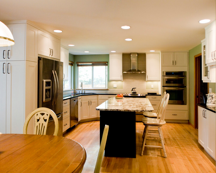 Example of a mid-sized transitional light wood floor kitchen design in Seattle with an undermount sink, recessed-panel cabinets, white cabinets, granite countertops, white backsplash, ceramic backsplash, stainless steel appliances and an island