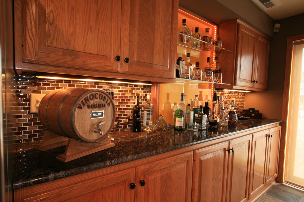 Photo of a mid-sized transitional single-wall wet bar in Minneapolis with raised-panel cabinets, medium wood cabinets, granite benchtops, glass tile splashback, multi-coloured splashback and slate floors.
