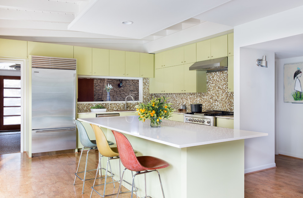 This is an example of a midcentury l-shaped kitchen in Austin with flat-panel cabinets, green cabinets, brown splashback, mosaic tile splashback, stainless steel appliances, with island and beige floor.