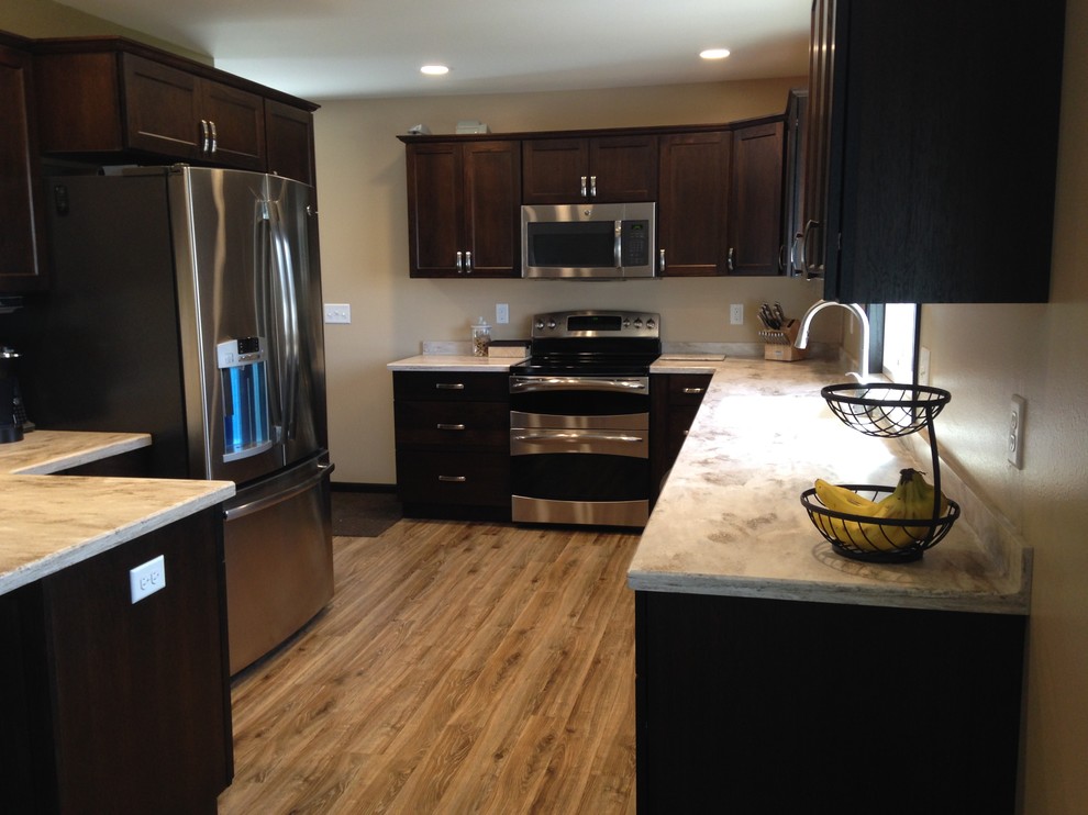 Enclosed kitchen - mid-sized transitional u-shaped medium tone wood floor enclosed kitchen idea with flat-panel cabinets, dark wood cabinets, solid surface countertops, stainless steel appliances, a peninsula and a drop-in sink