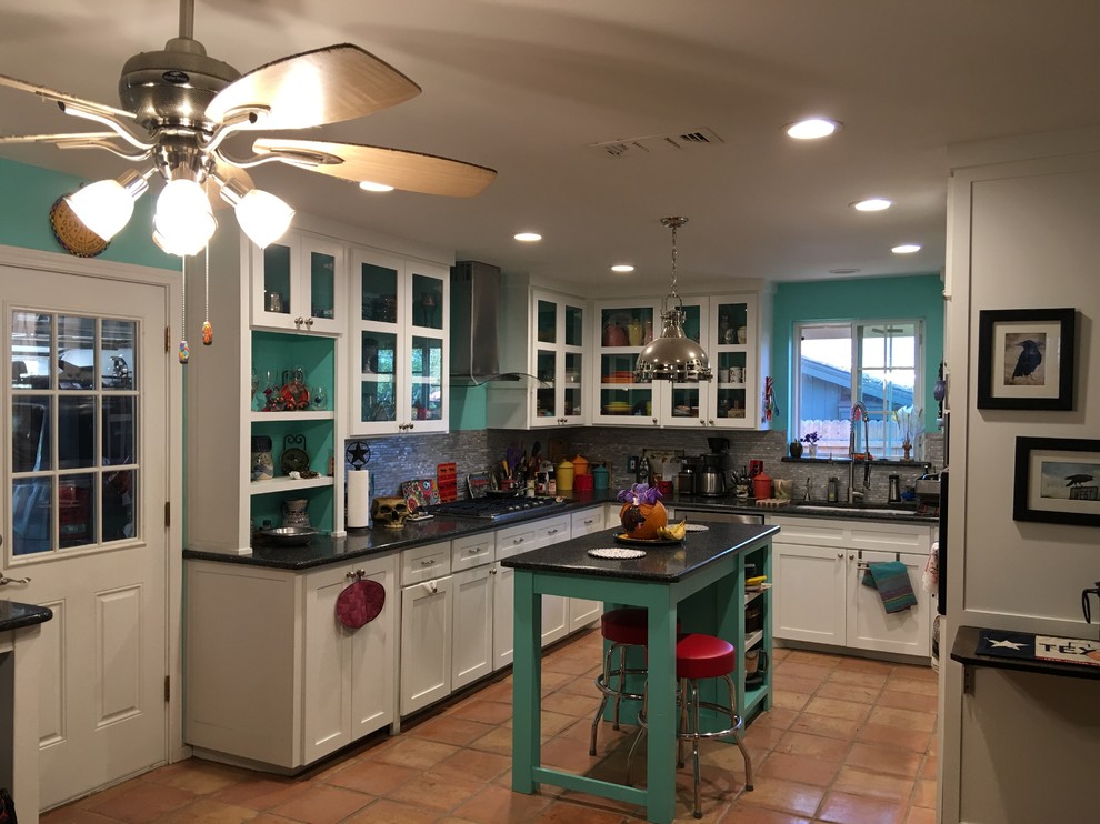 Mid-sized eclectic u-shaped open plan kitchen in Dallas with an undermount sink, glass-front cabinets, white cabinets, granite benchtops, grey splashback, glass tile splashback, stainless steel appliances, terra-cotta floors, with island and beige floor.