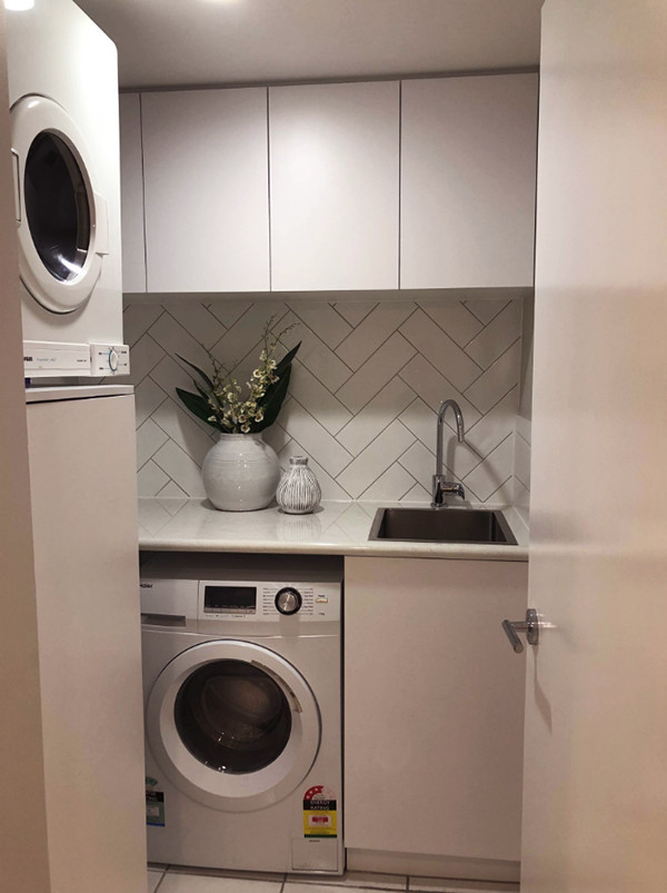 Inspiration for a small transitional l-shaped dedicated laundry room in Brisbane with a single-bowl sink, flat-panel cabinets, white cabinets, laminate benchtops, grey walls, ceramic floors and white floor.